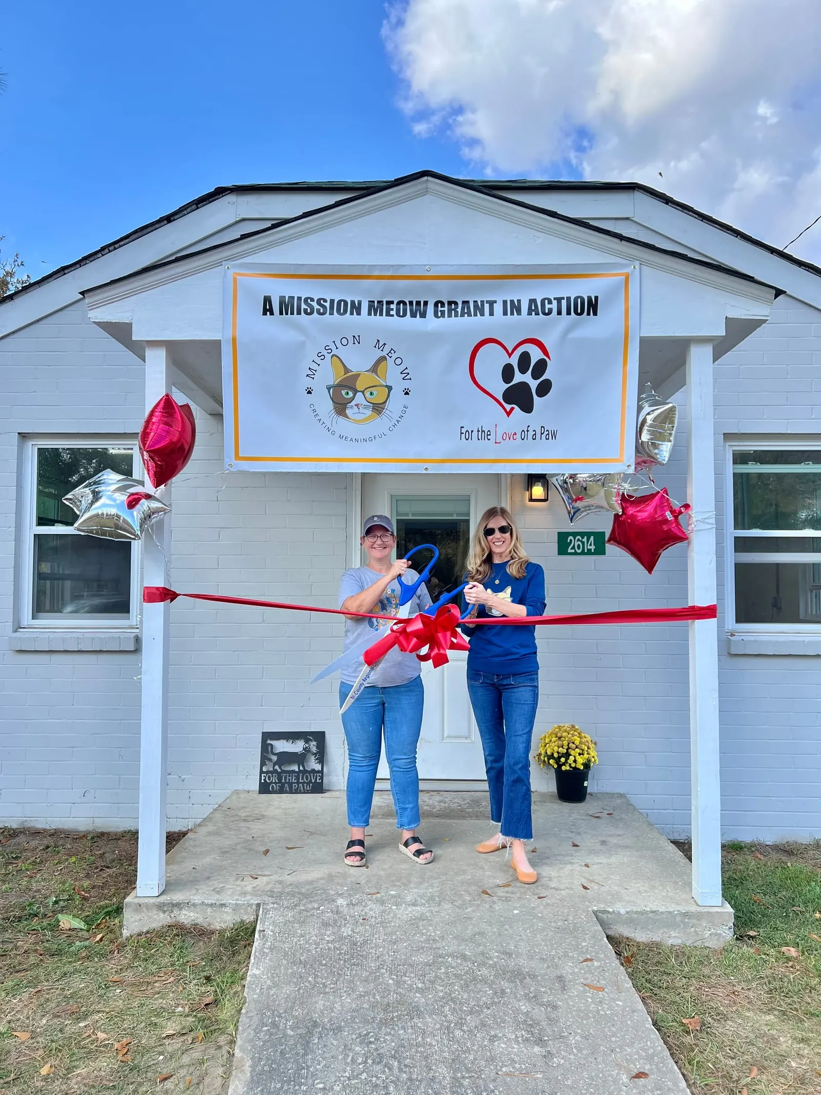 A ribbon cutting outside a small house with a banner reading “A Mission Meow Grant in Action”