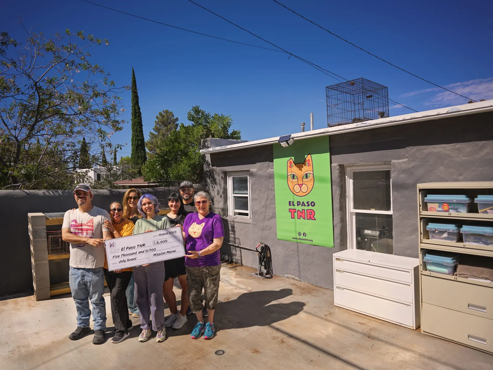 The El Paso TNR group holds its Mission Meow check outside their cat facility under a blue sky