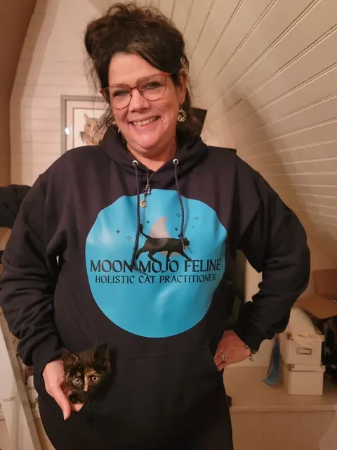 Lora Lee Medley in a Moon Mojo Feline hoodie, with a tortoiseshell kitten peeking out of its pocket