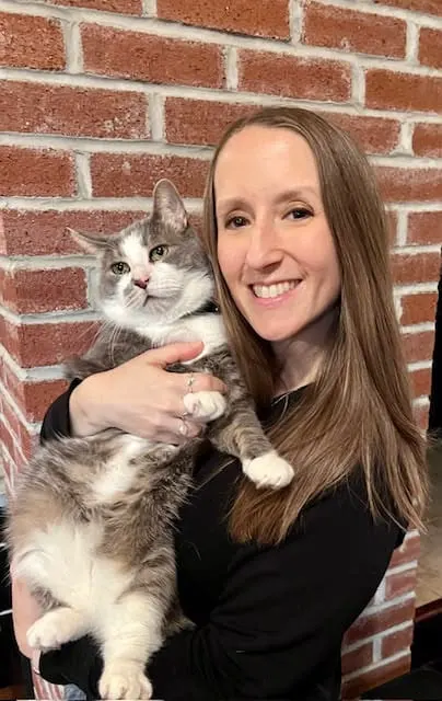 Trisha Counterman holding a gray-and-white cat in front of a brick wall