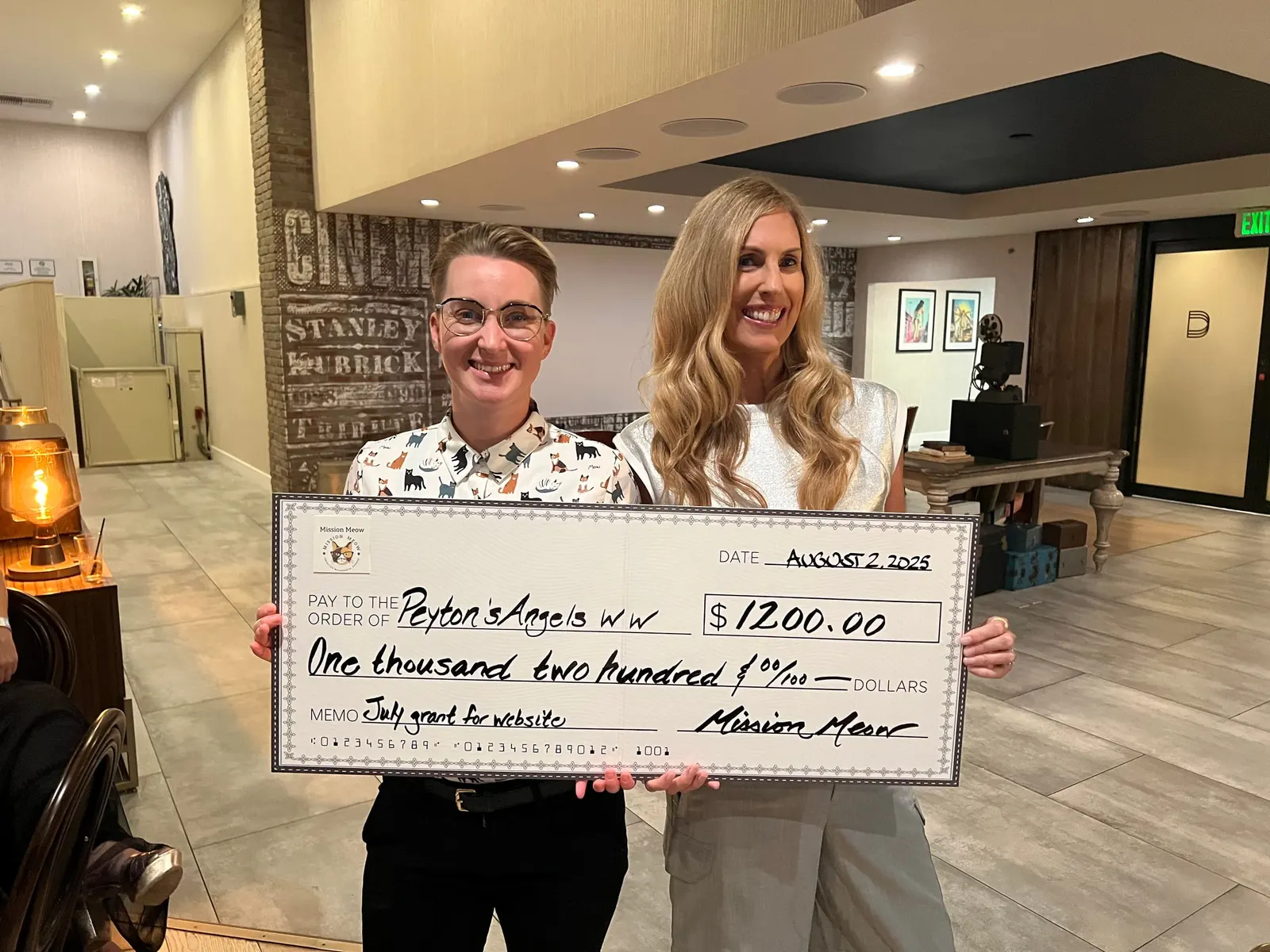 Two people hold a $1,200 check made out to Peyton’s Angels